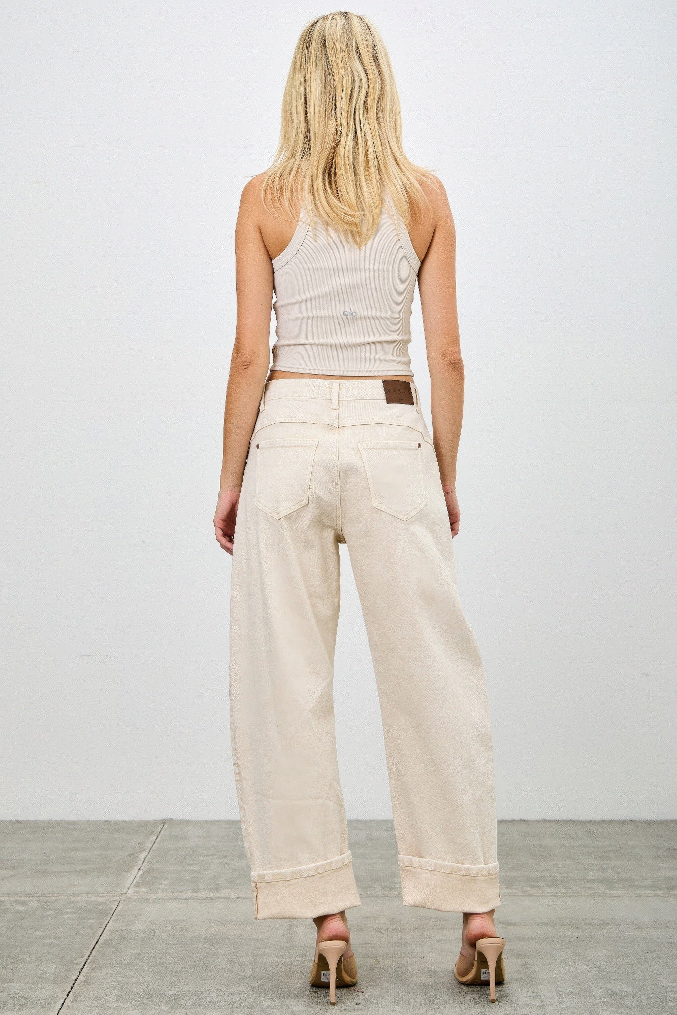 Woman wearing a white sleeveless top and beige western barrel jeans butt view