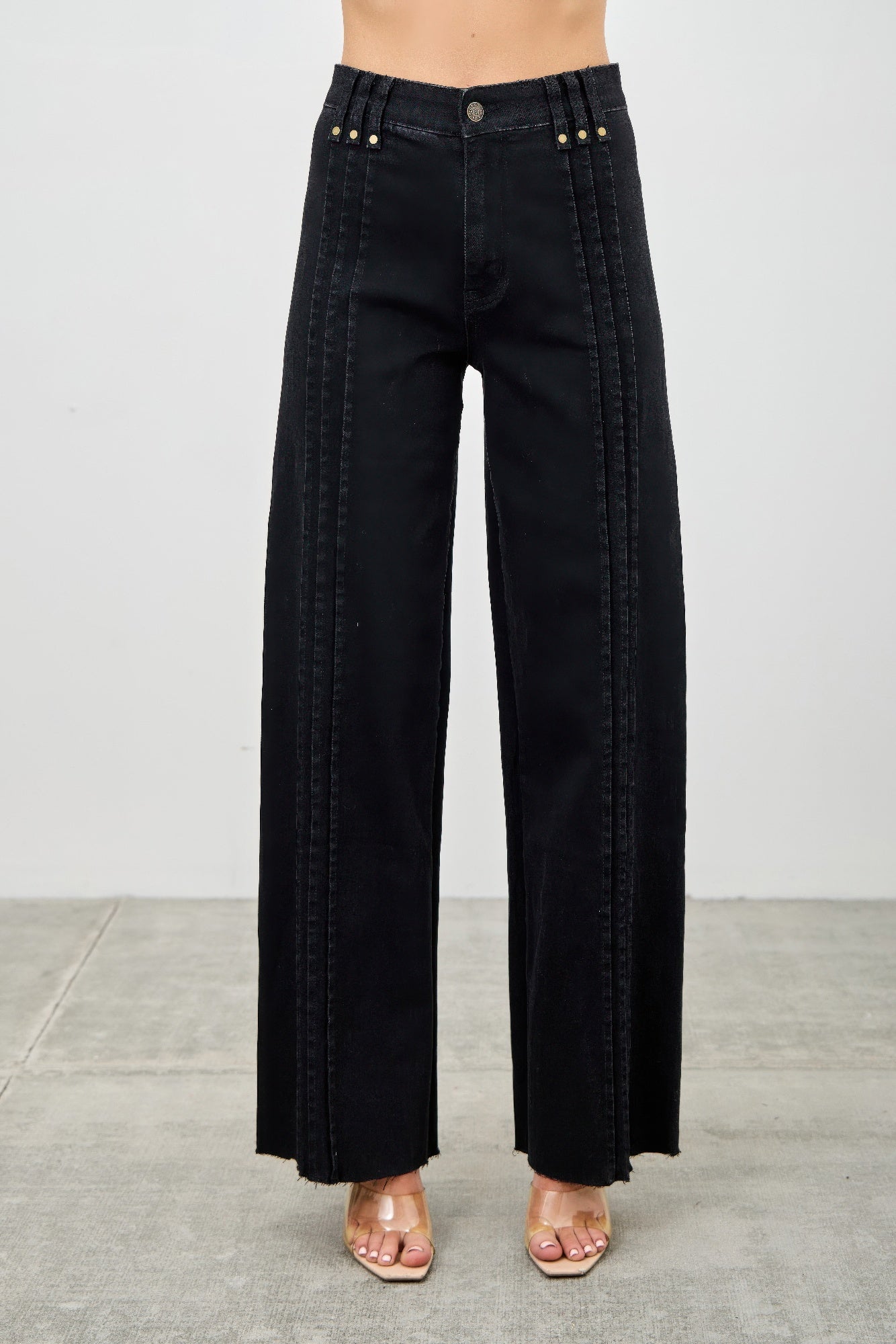 Black wide-leg jeans worn by a person on a gray background detail view