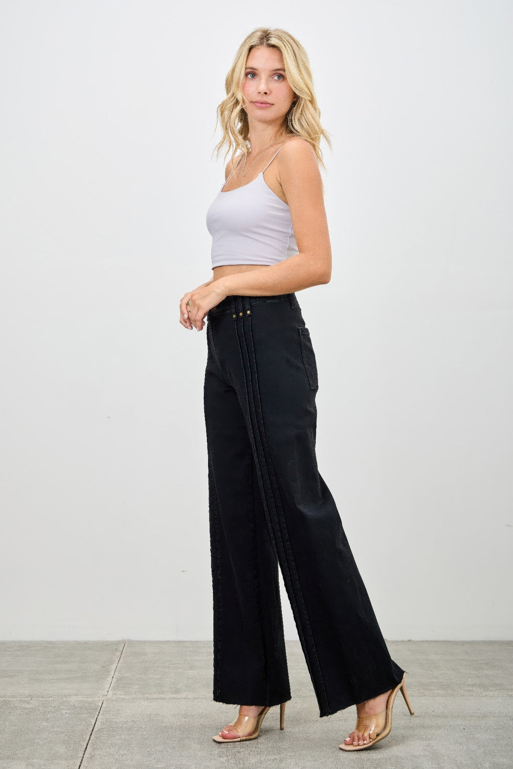 Woman wearing a light gray tank top and black wide-leg pants on a white background side view