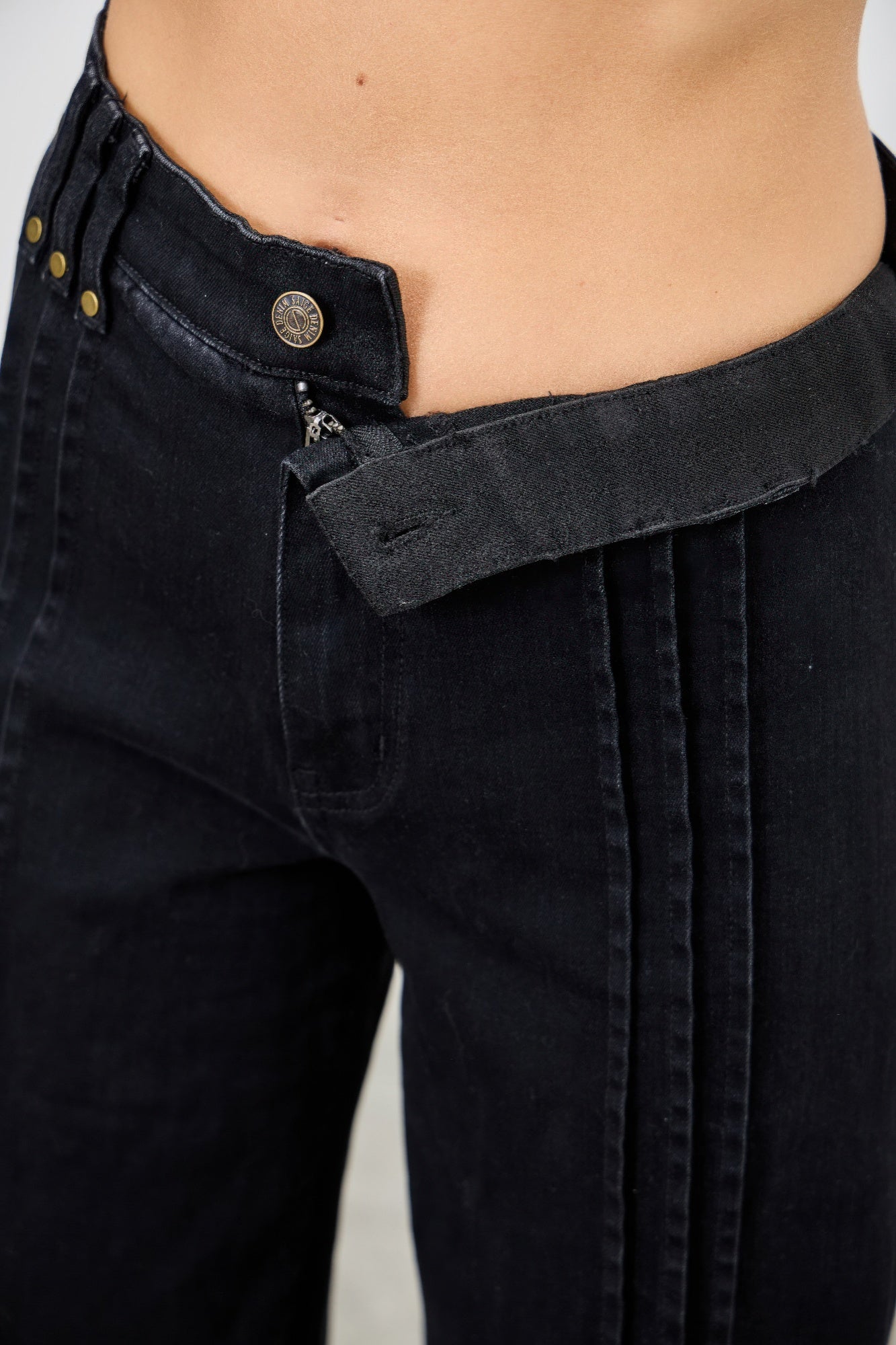 Close-up of black pants with a focus on the waistband and zipper. Waist view