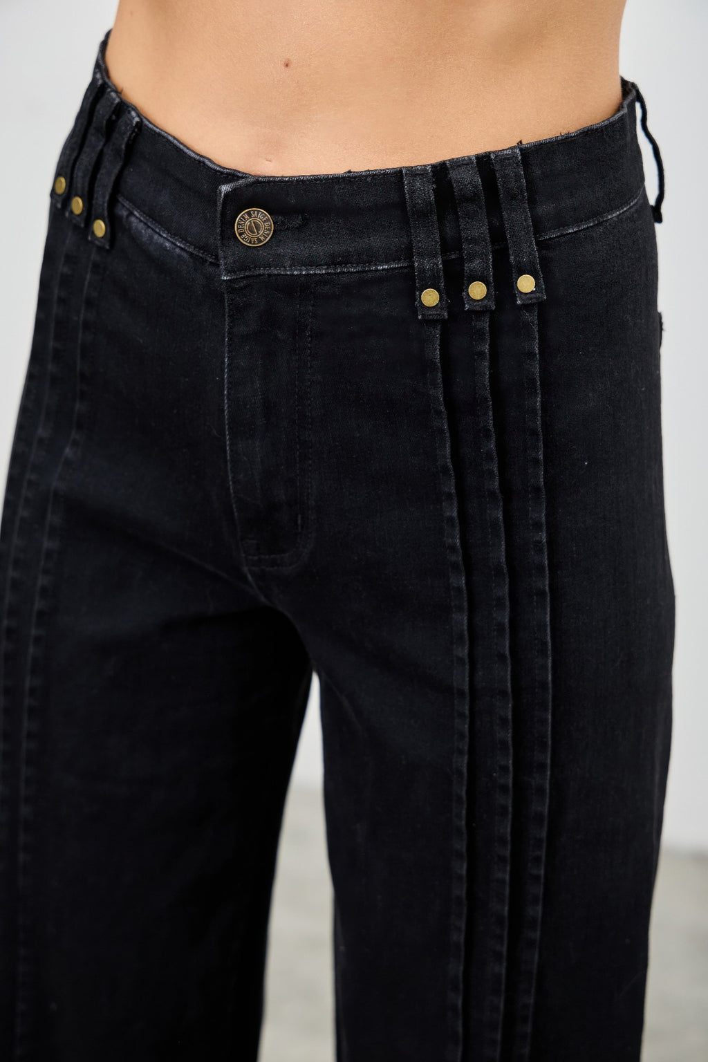 Close-up of black jeans with gold buttons and zippers on a plain background detailed waist view