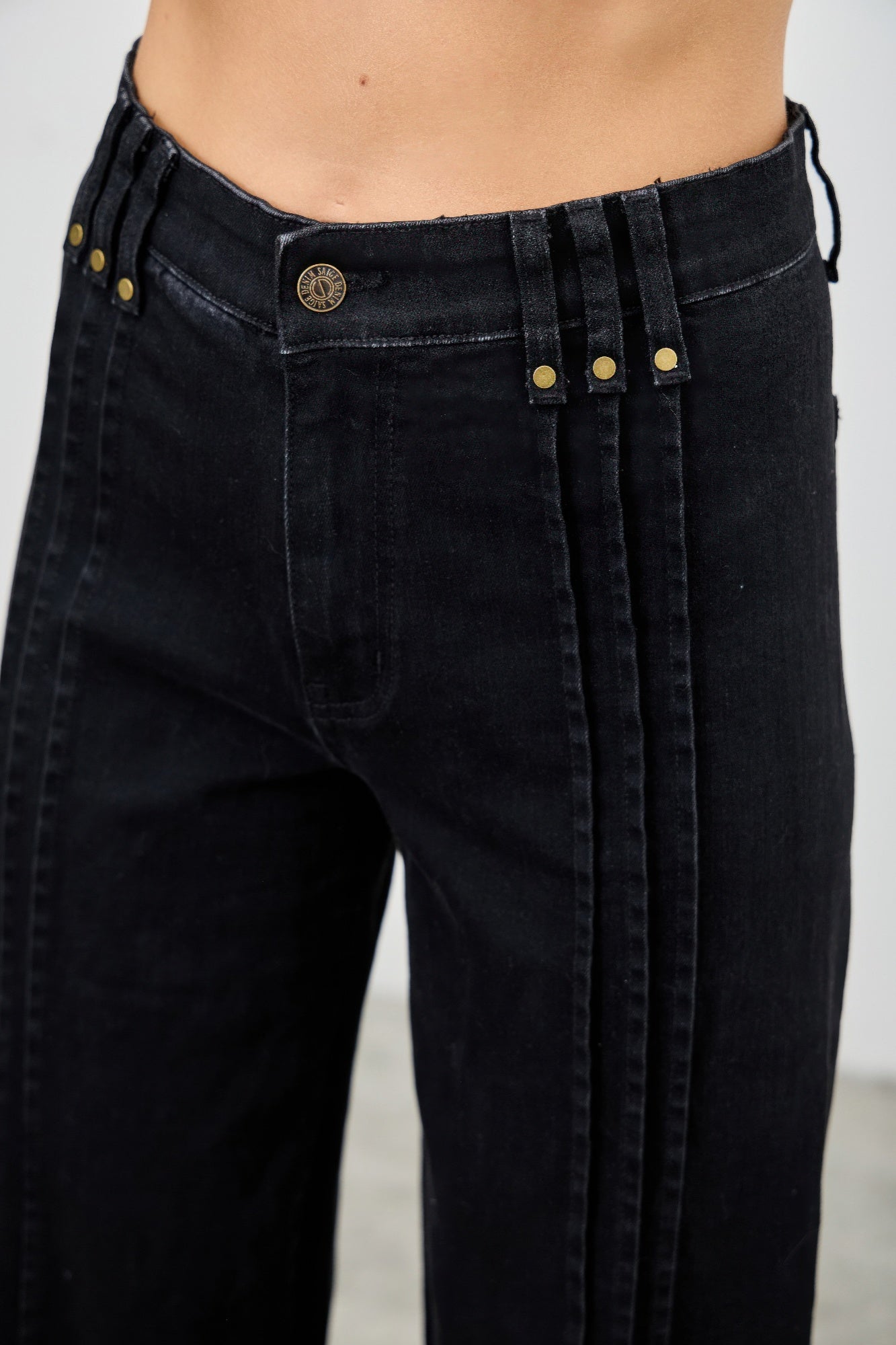 Close-up of black jeans with gold buttons and zippers on a plain background detailed waist view