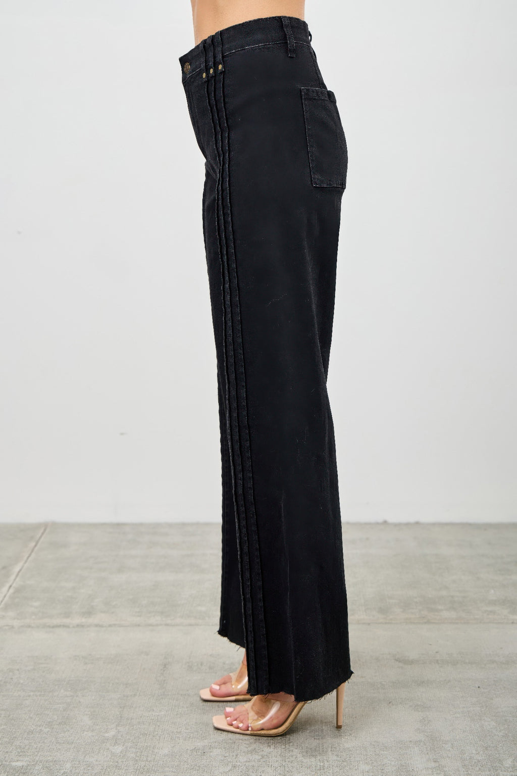 Black wide-leg jeans worn by a person on a gray floor. Detailed side view