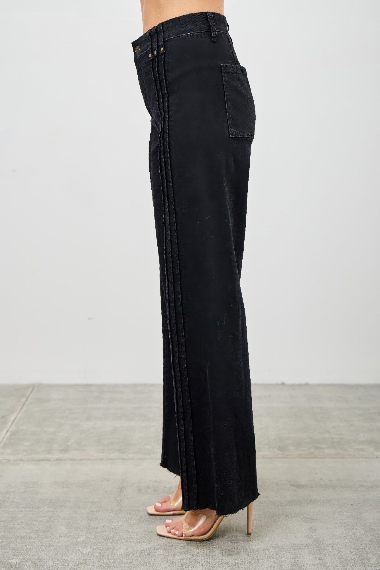 Black wide-leg jeans worn by a person on a gray floor. Detailed side view