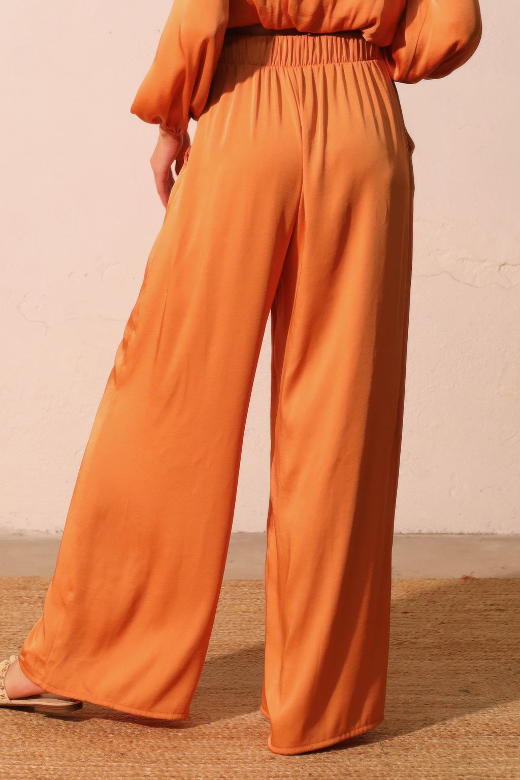 Person wearing orange pants against a beige wall back view