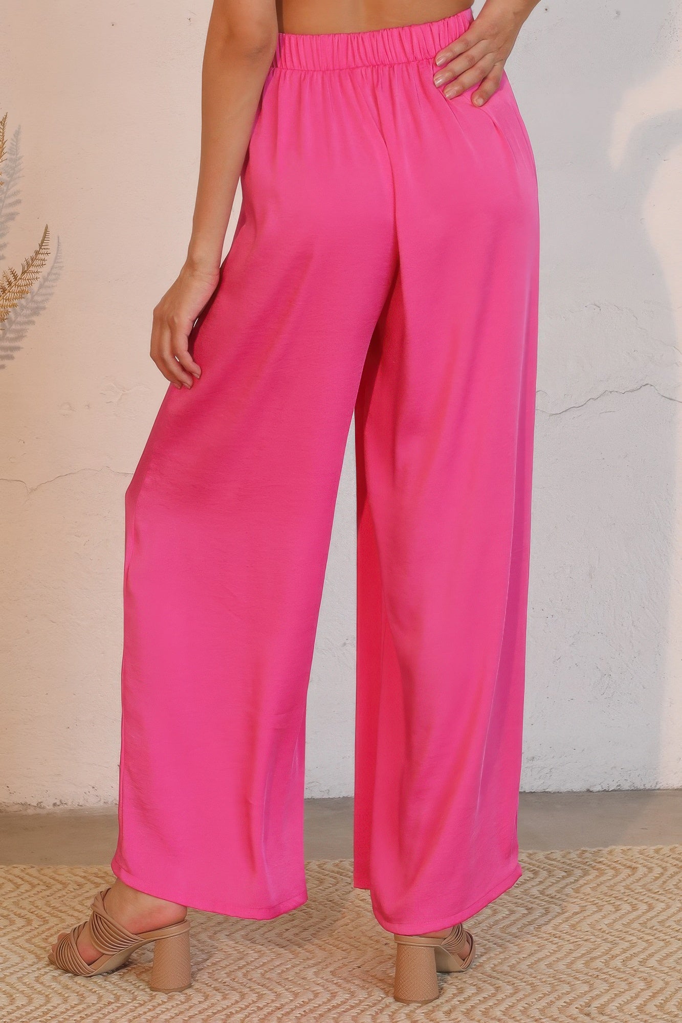 Person wearing bright pink wide-leg pants against a neutral background back view