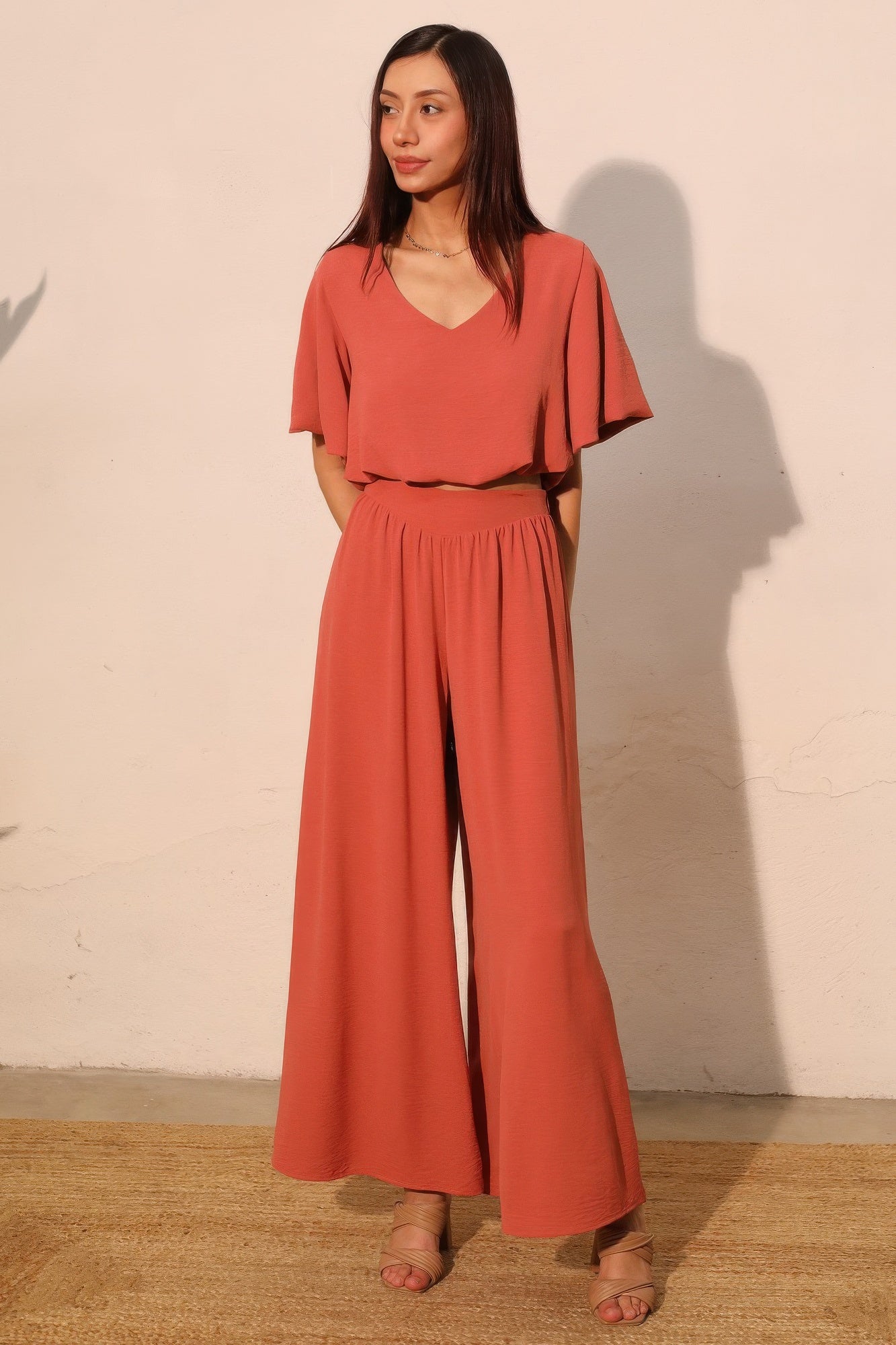 Woman wearing a coral jumpsuit standing against a plain wall. Front view