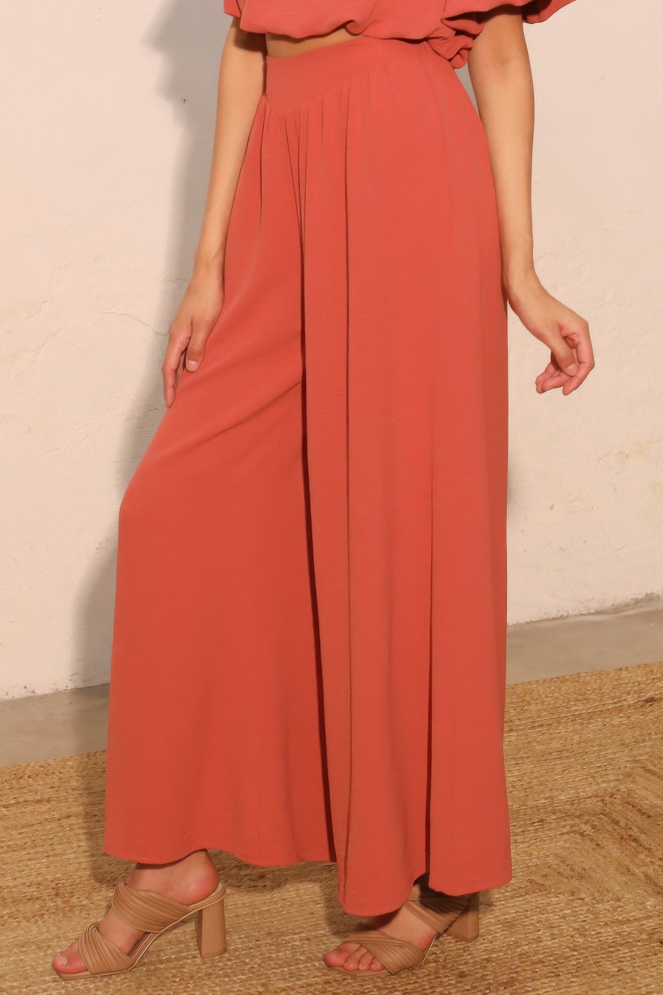 Person wearing a coral outfit with wide-leg pants and a top on a neutral background close-up