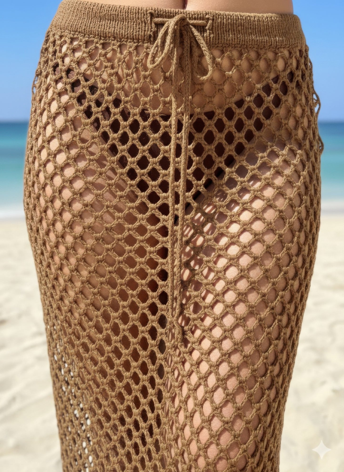 Brown crochet skirt on a beach with blue water and sky cloe-up.