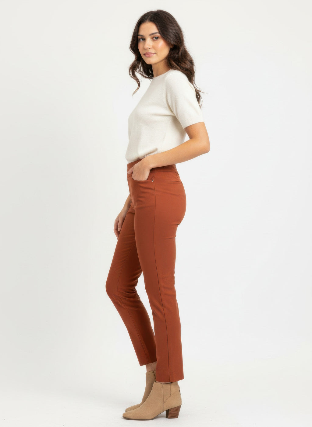 Woman wearing a white top and brown pants on a white background side view