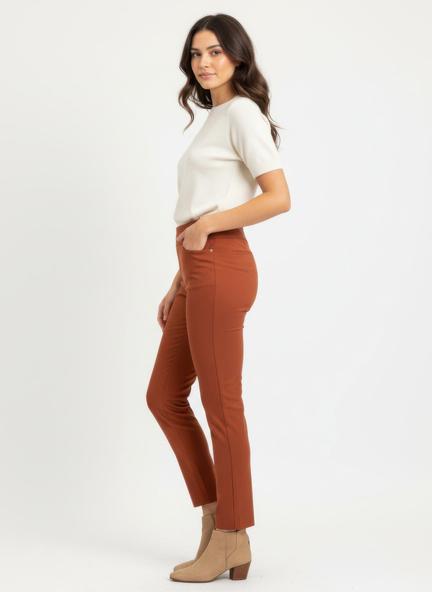 Woman wearing a white top and brown pants on a white background side view