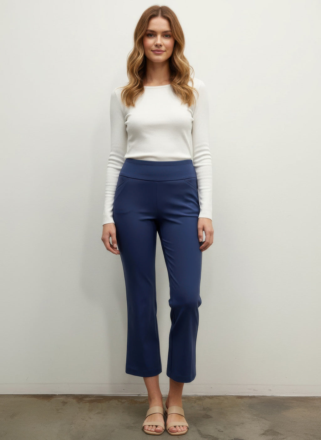 Woman wearing a white top and blue pants against a plain background front view