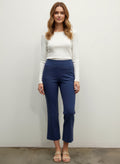 Woman wearing a white top and blue pants against a plain background front view