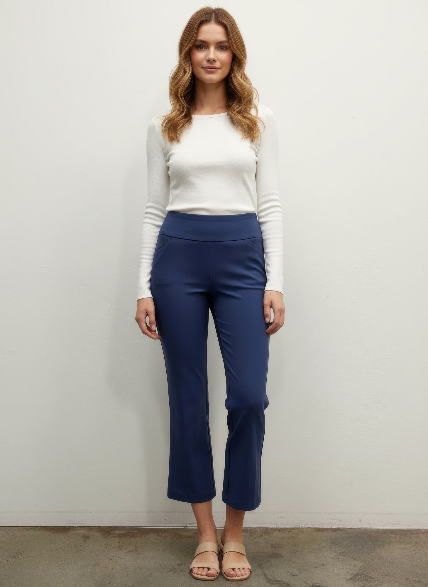 Woman wearing a white top and blue pants against a plain background front view