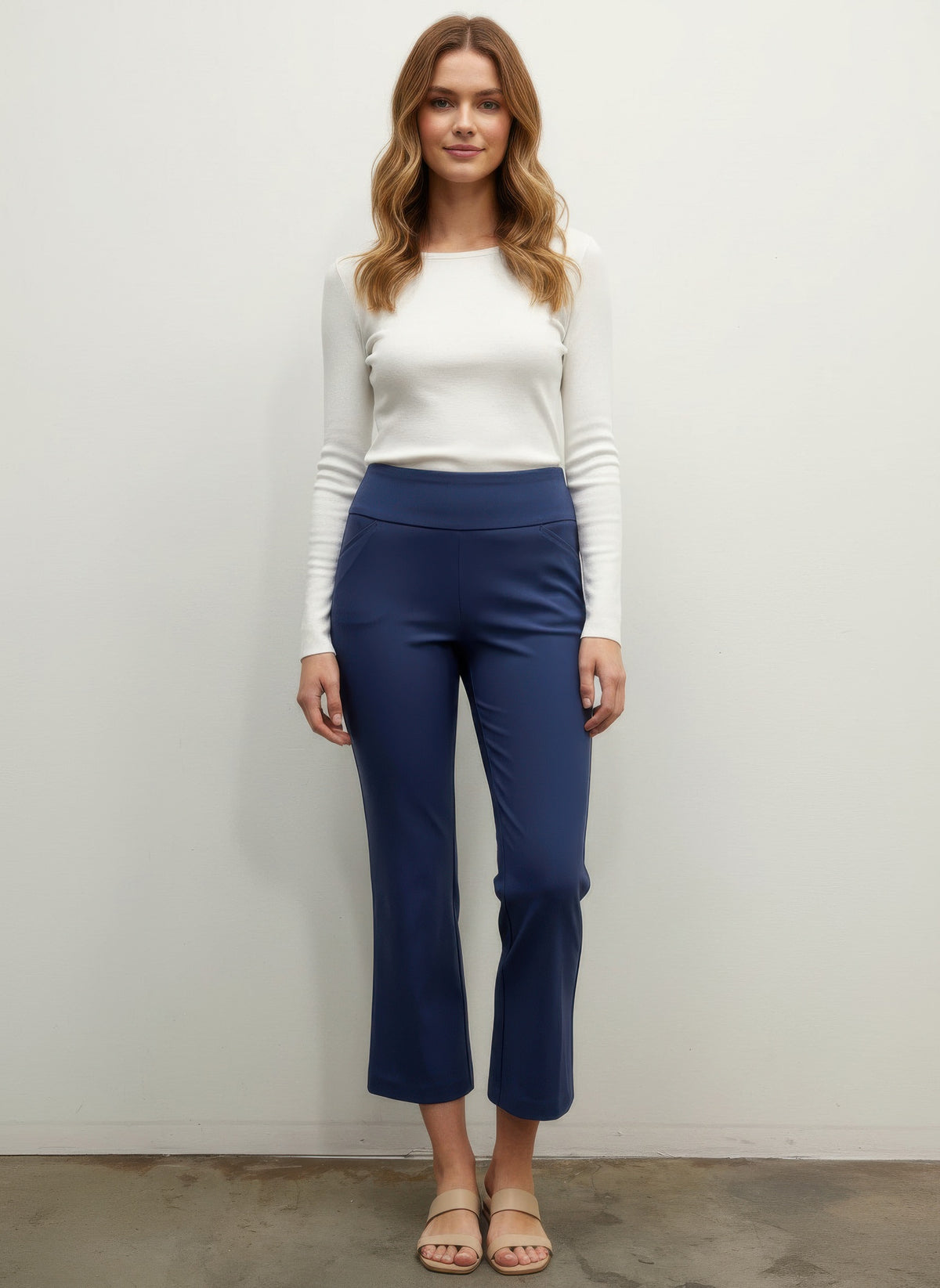 Woman wearing a white top and blue pants against a plain background front view