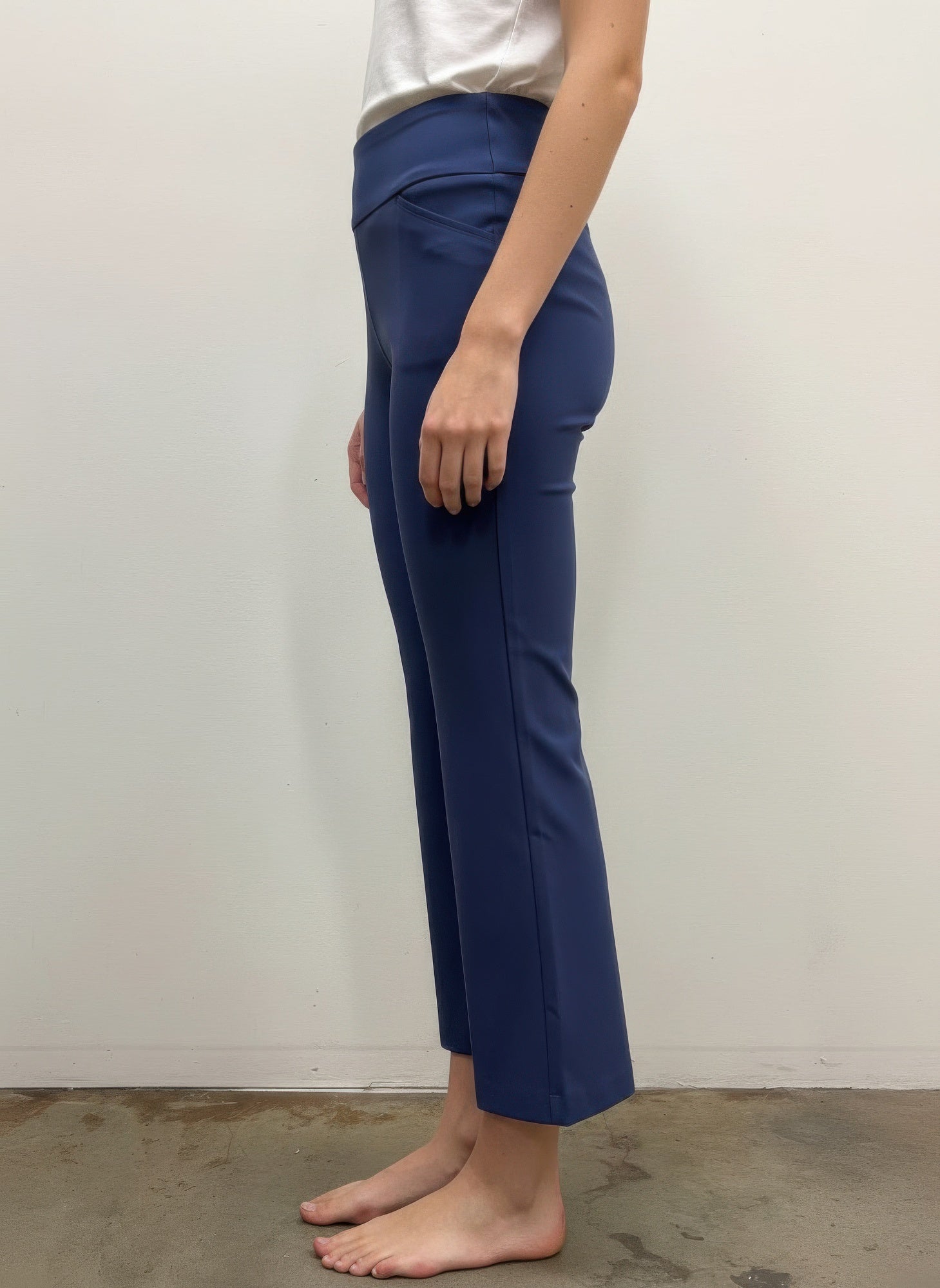 Person wearing blue pants standing against a plain white wall. Side view