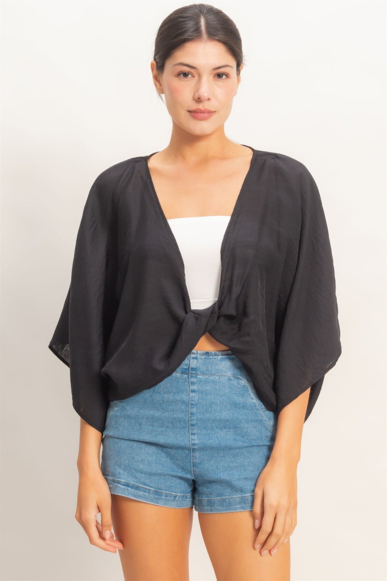 Woman wearing a black oversized twist knot cardigan over a white top and blue shorts 