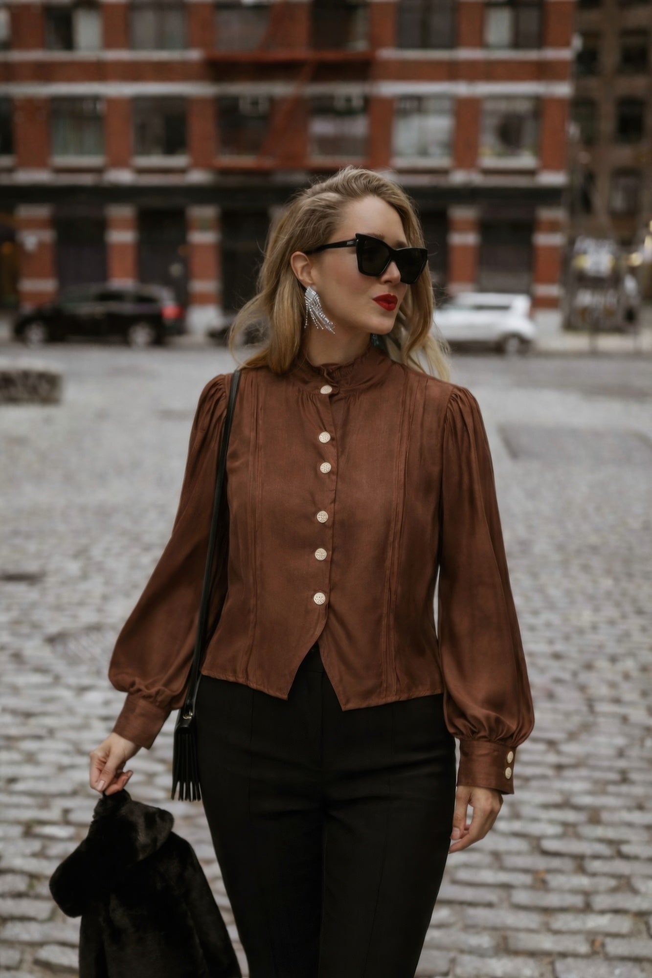 Woman wearing a brown Victorian blouse with a high collar and buttons, standing on a street.