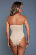 Woman wearing a beige strapless bodysuit against a gray background