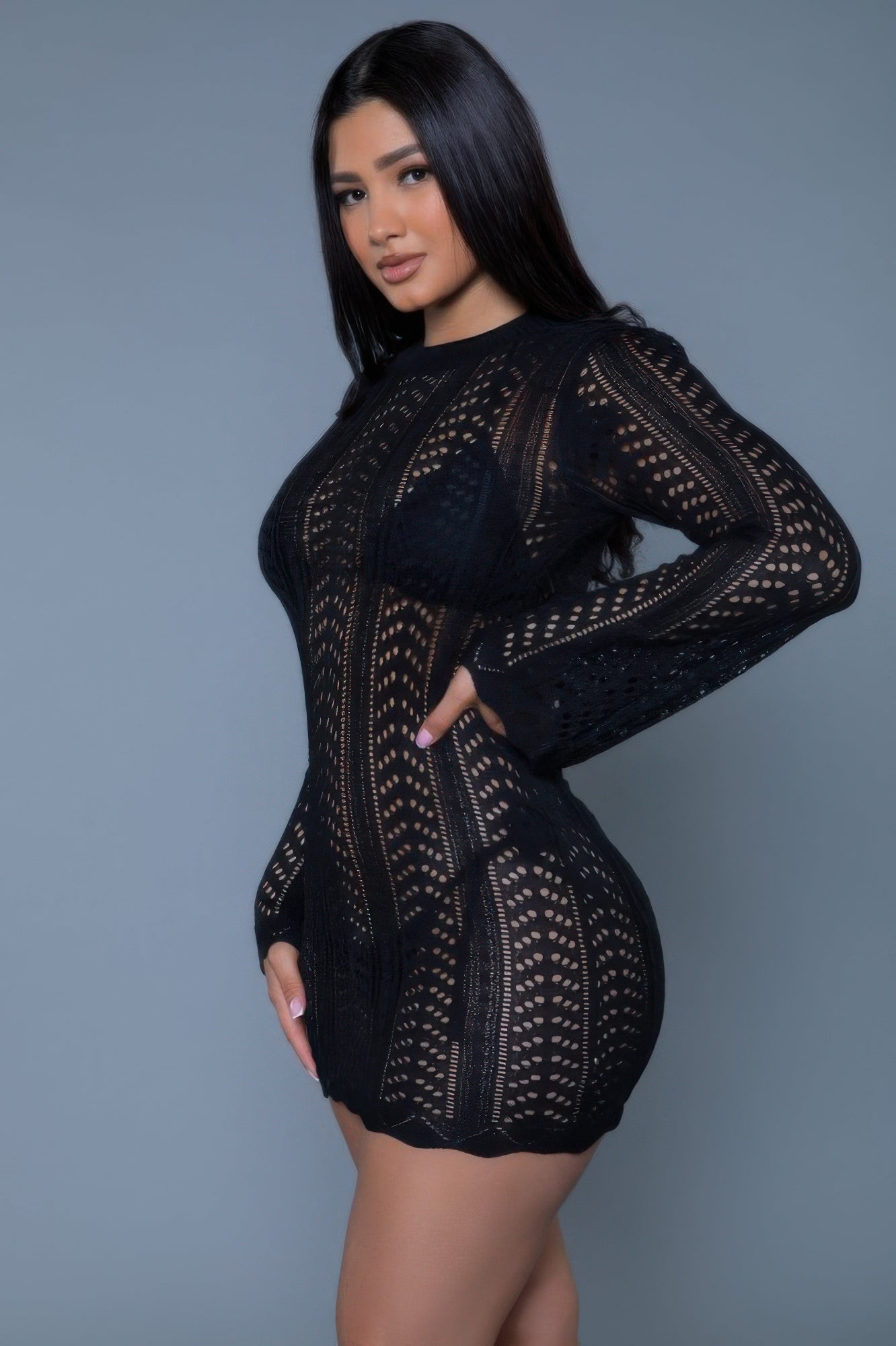 Woman wearing a black lace dress against a gray background side view