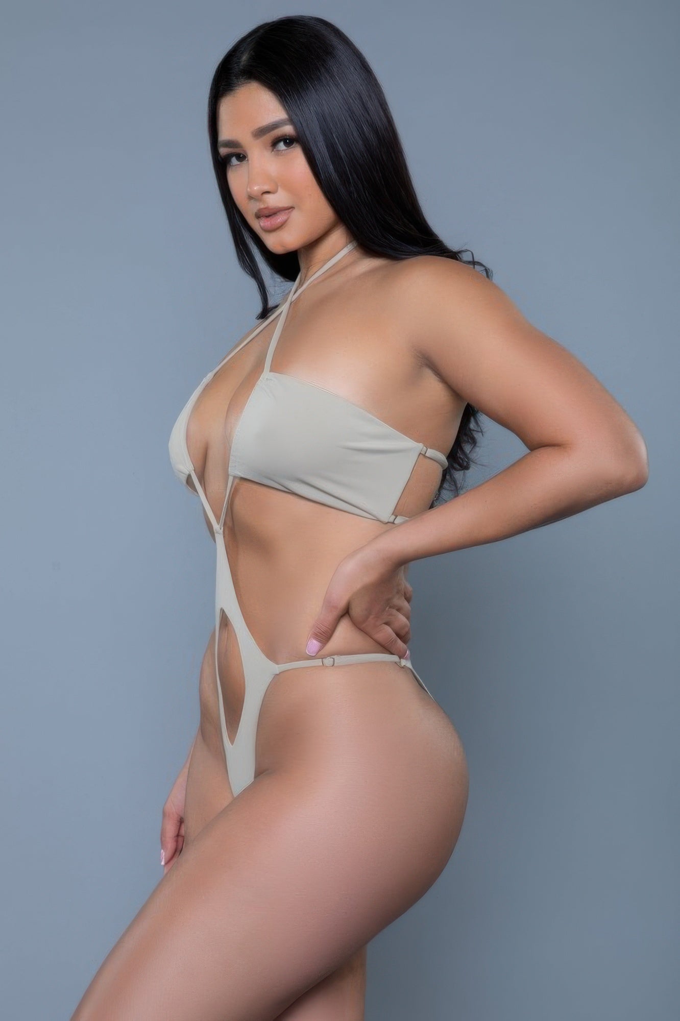 Woman wearing a beige bikini against a gray background side view.