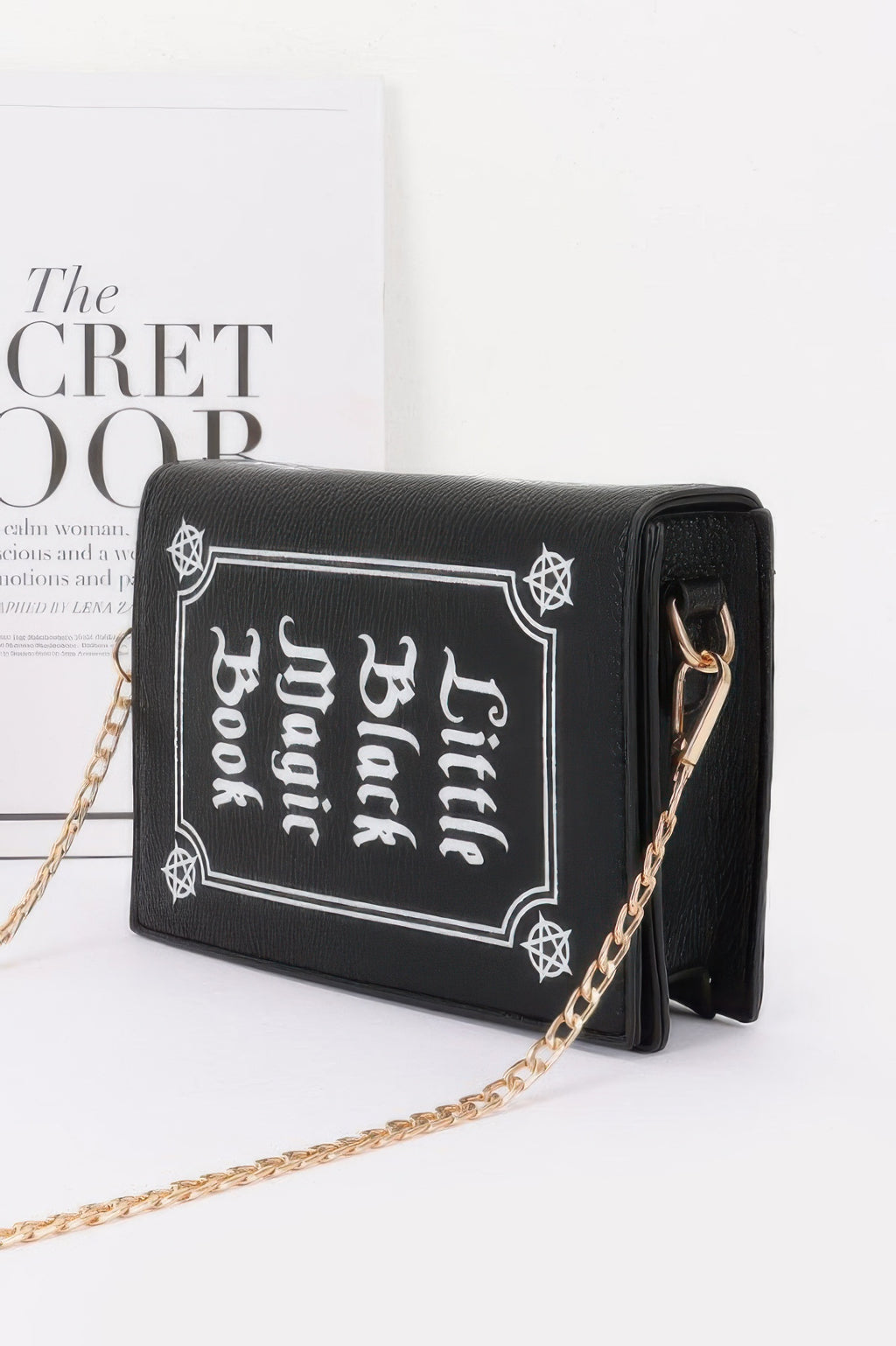 Black handbag with 'Little Black Magic Book' design and gold chain angle view