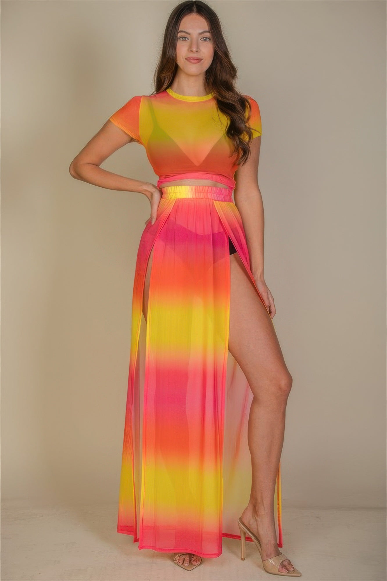 Woman wearing a colorful maxi dress with a gradient of red, orange, and yellow on a beige background