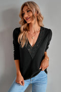Woman wearing a black v-neck  blouse with lace details and blue jeans against a gray background