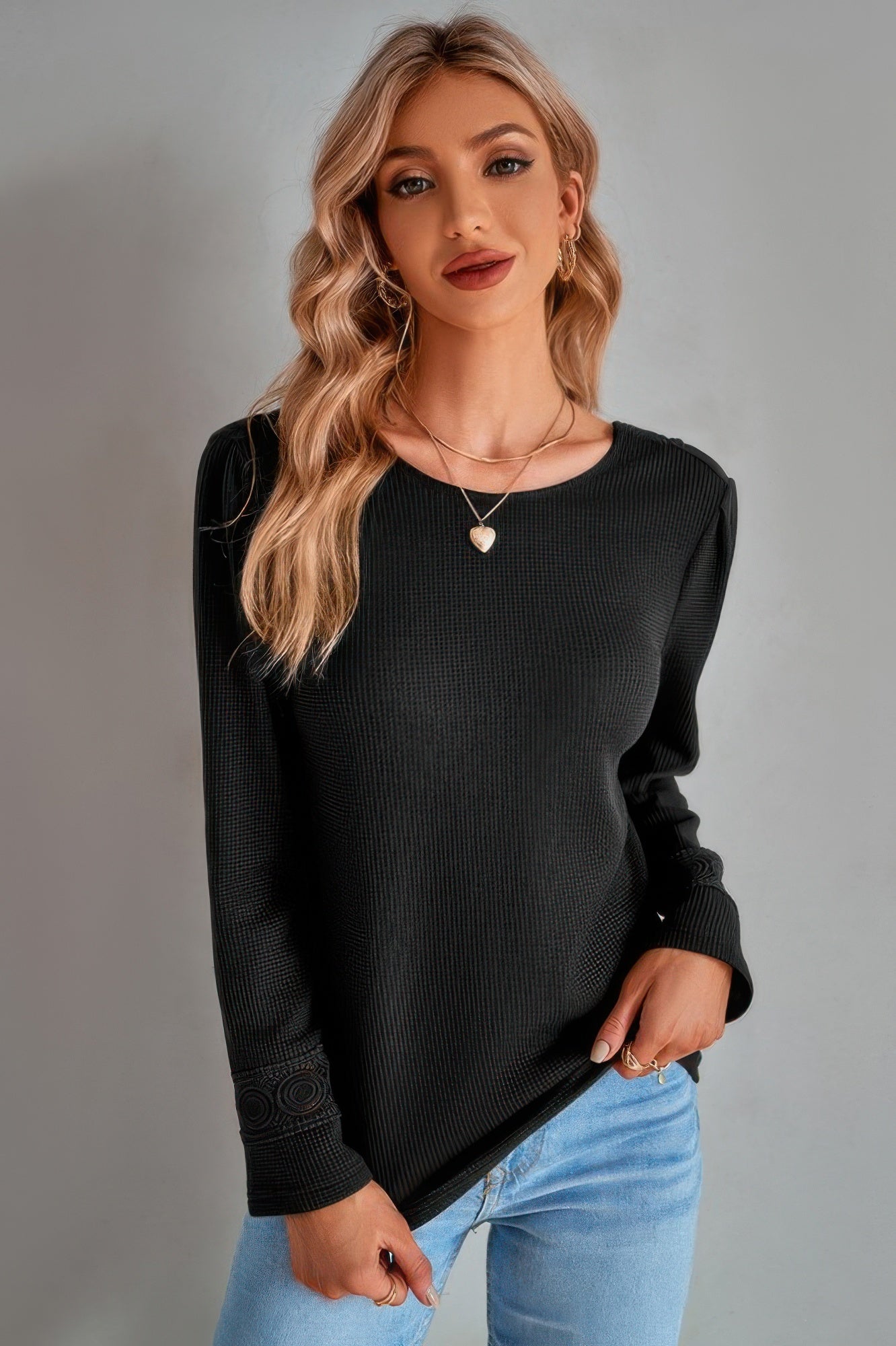 Woman wearing a black bidirectional blouse and blue jeans against a gray background