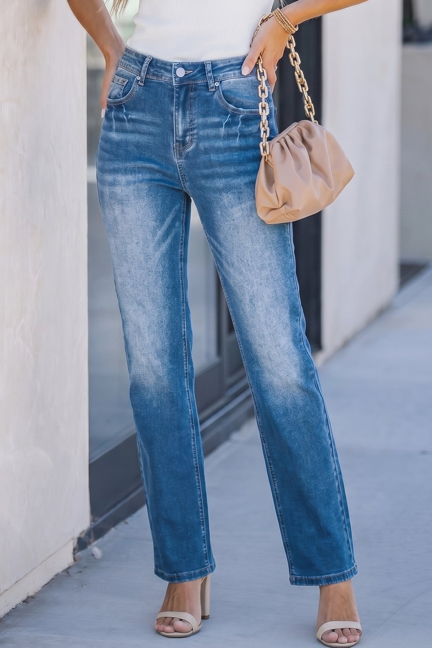 Person wearing blue jeans and a beige handbag on a sidewalk. Front view
