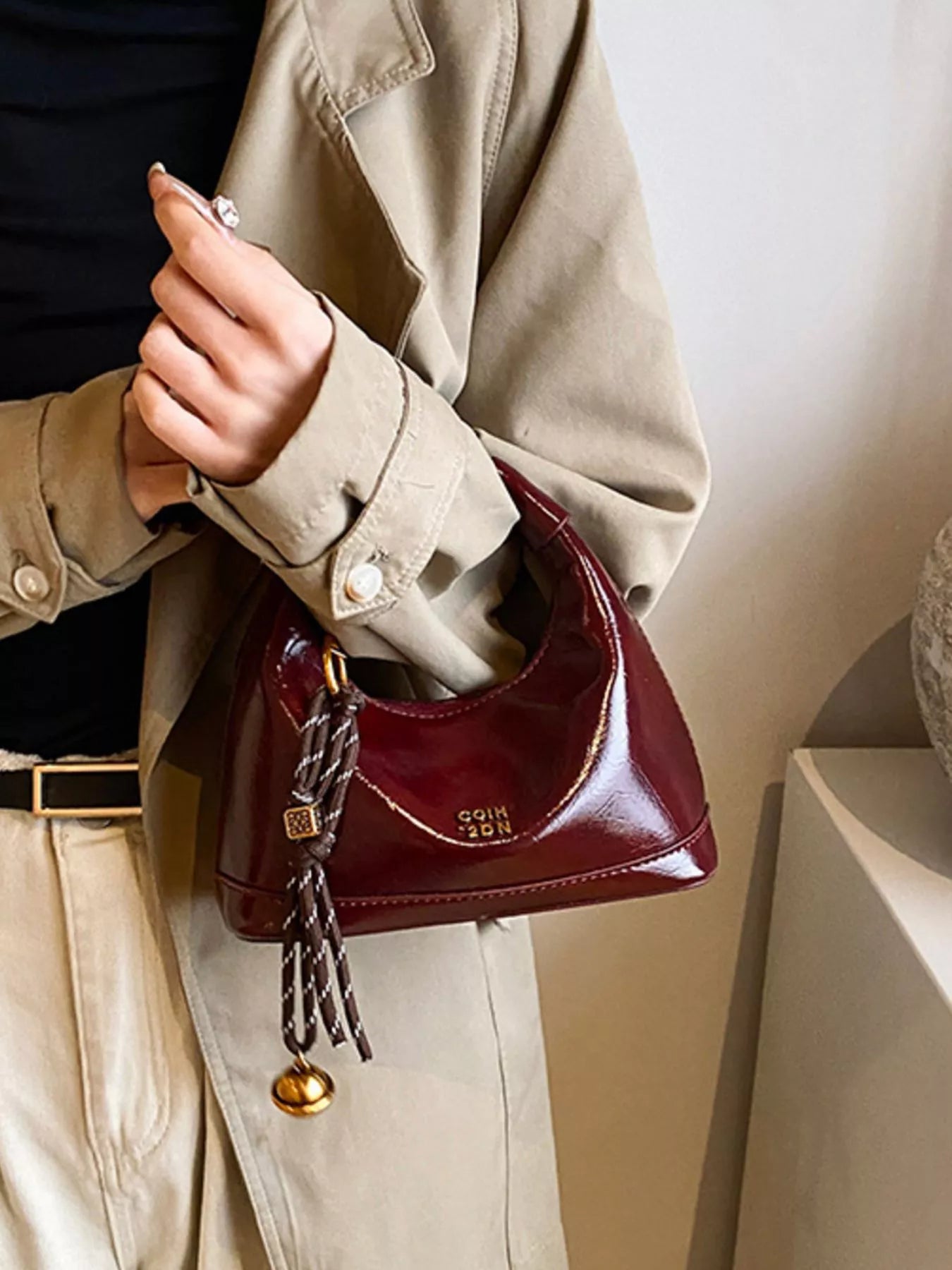 Person holding a burgundy handbag with decorative tassel against a neutral background