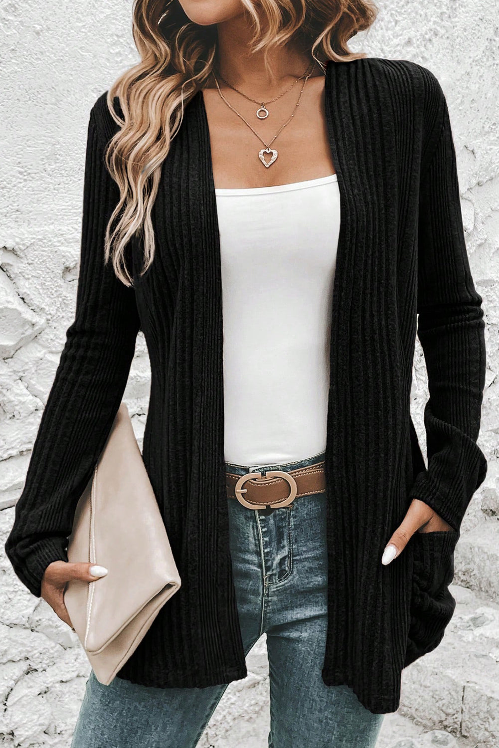 Person wearing a black cardigan over a white top and blue jeans, holding a beige clutch.