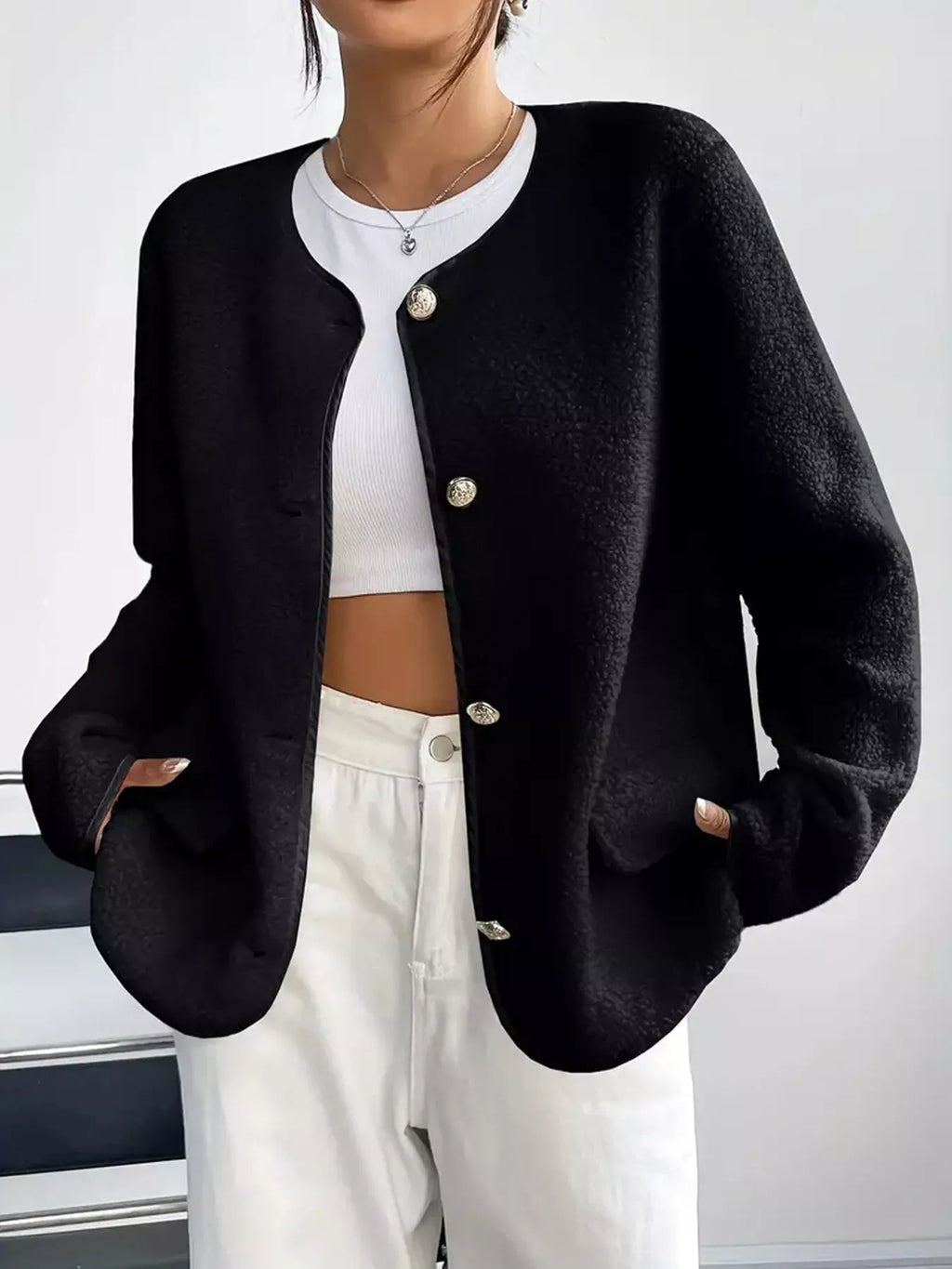 Person wearing a black cardigan over a white top and pants on a plain background