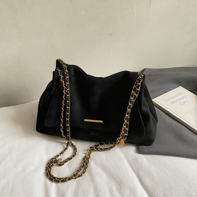 Black handbag with gold chain strap on a light surface
