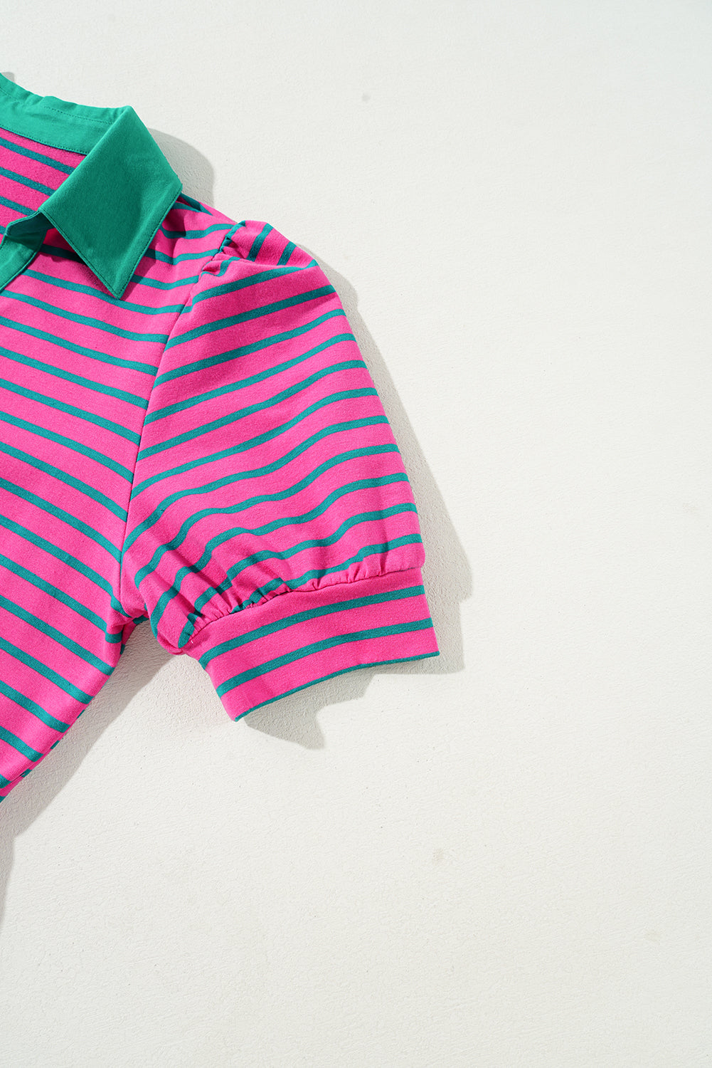 Pink and green striped baby romper on a light gray background