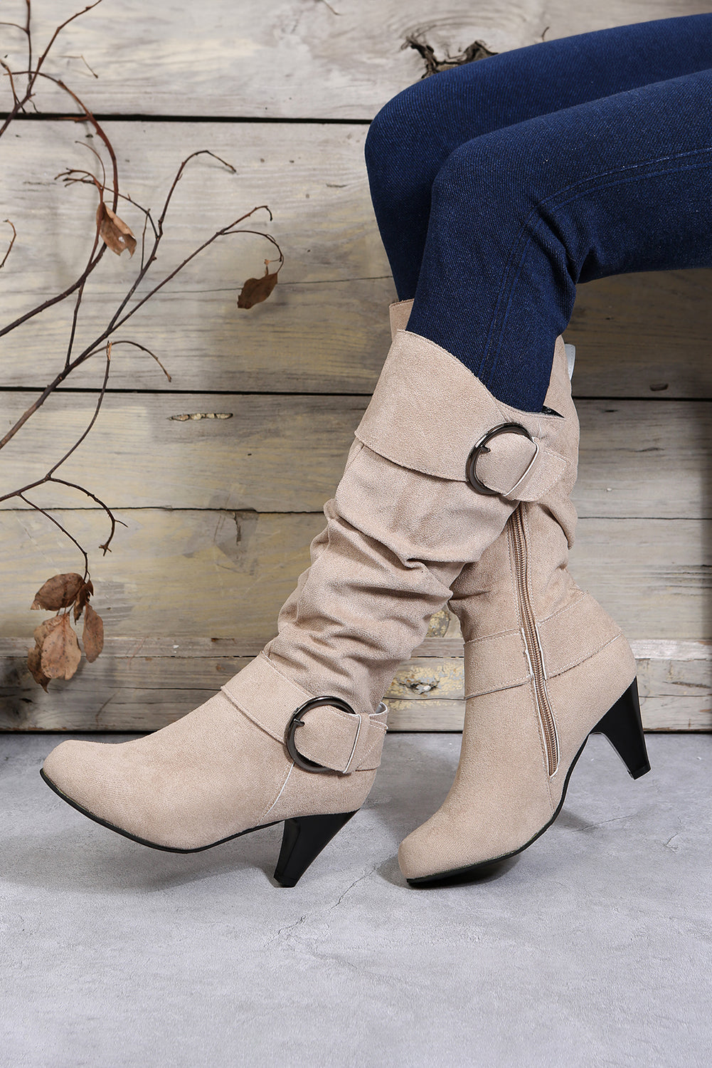 Beige knee-high boots with a buckle detail worn by a person against a wooden background.
