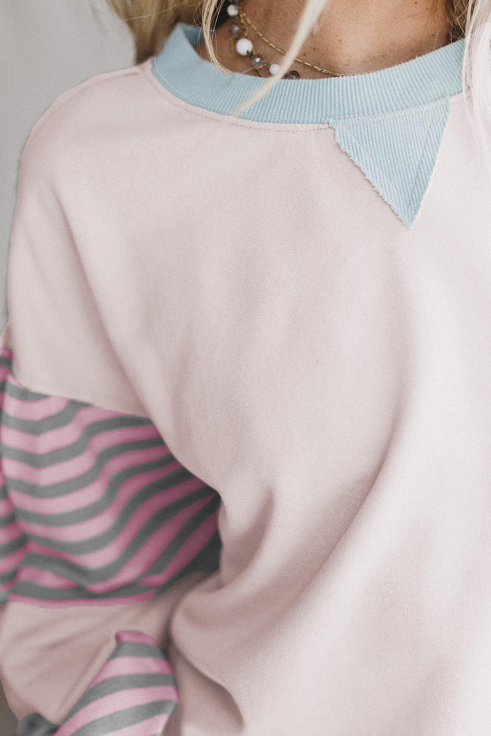 Close-up of a person wearing a light pink sweater with a blue collar and striped sleeves.
