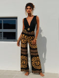 Woman wearing a black and gold patterned jumpsuit standing against a white wall. Front view