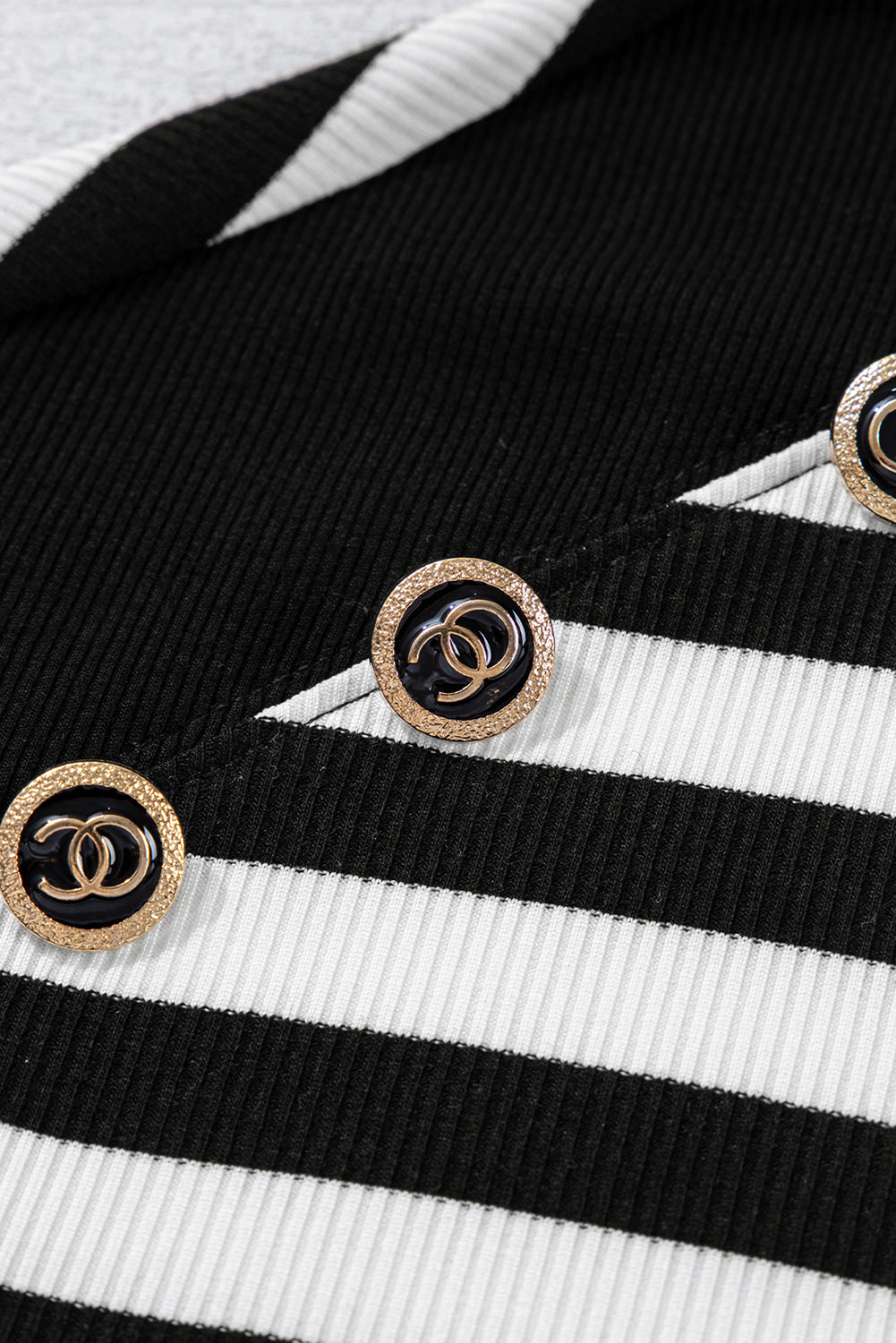 Close-up of a black and white striped fabric with gold buttons featuring the Chanel logo.