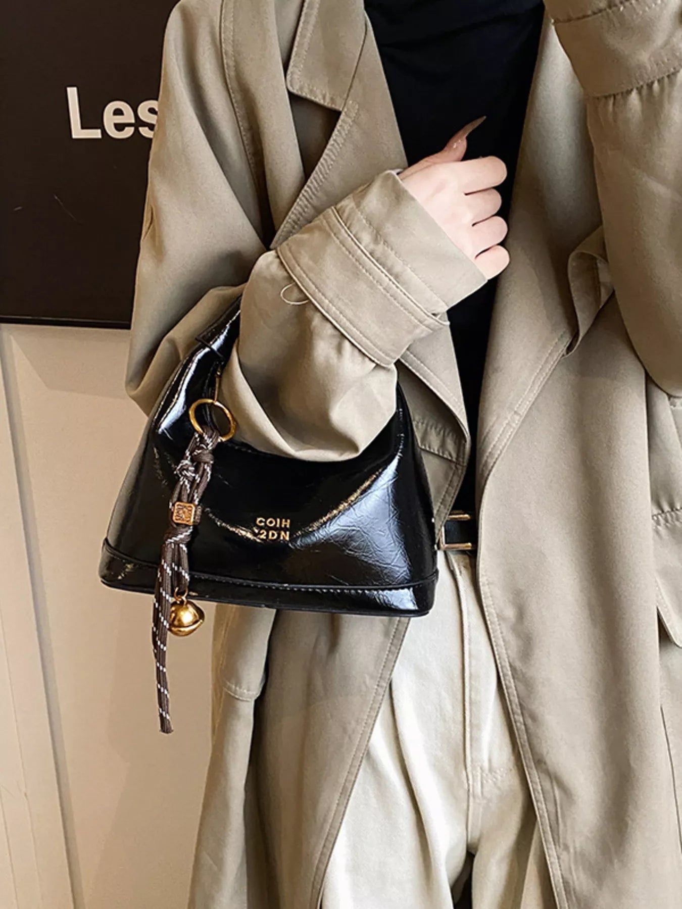 Person holding a black handbag with a beige coat