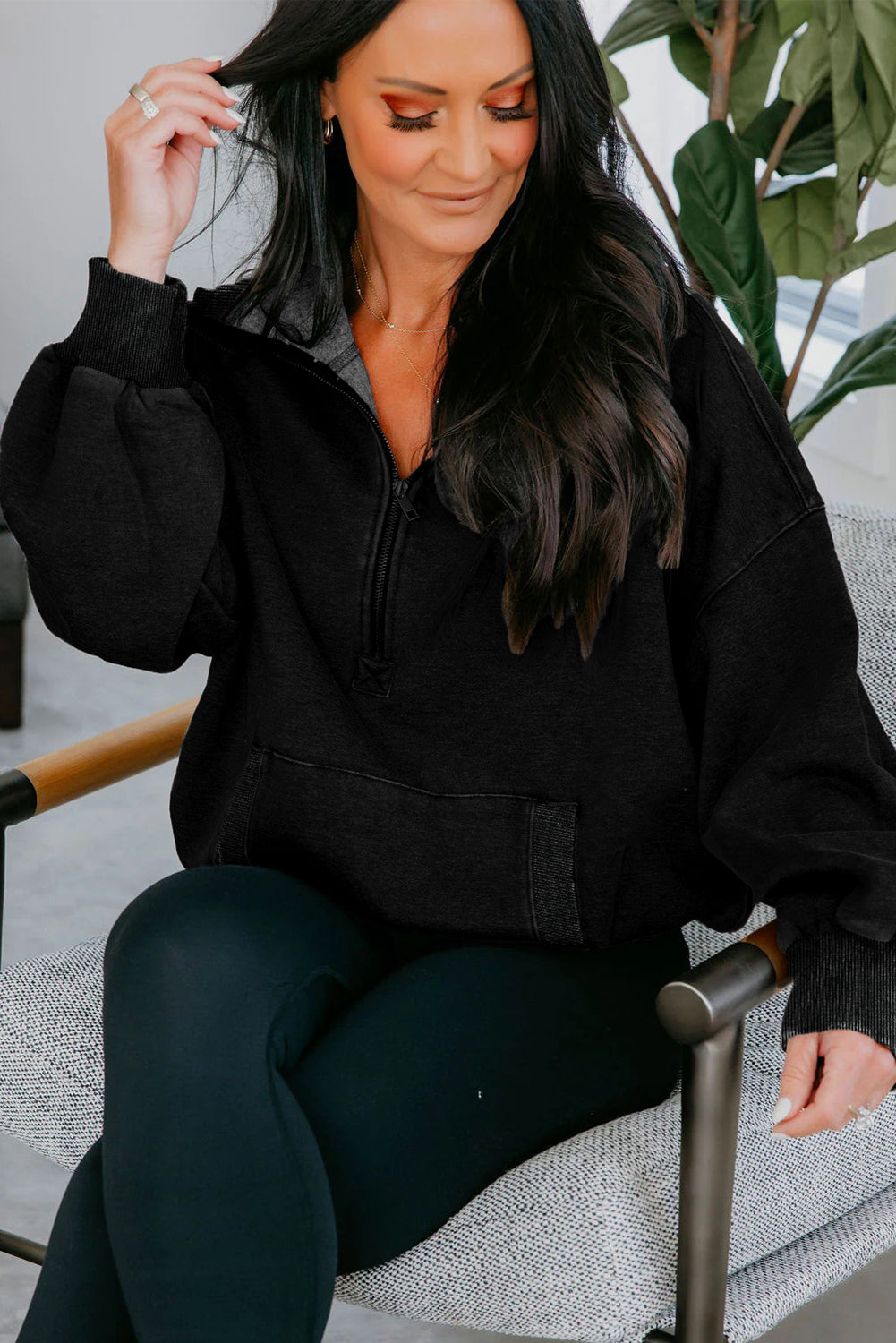 Woman wearing a black jacket sitting on a chair with plants in the background