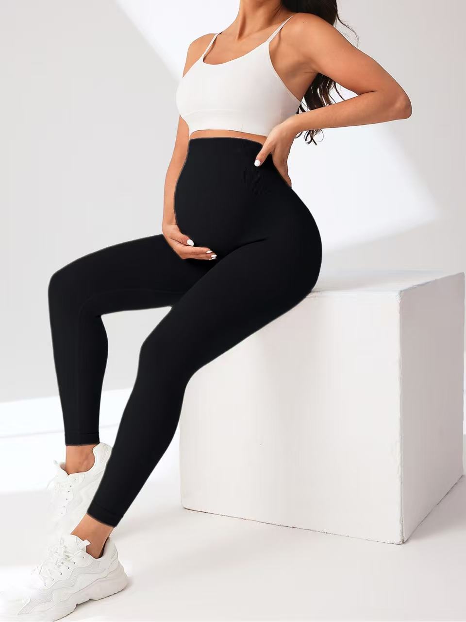 Person wearing black leggings and a white sports bra sitting on a white box.