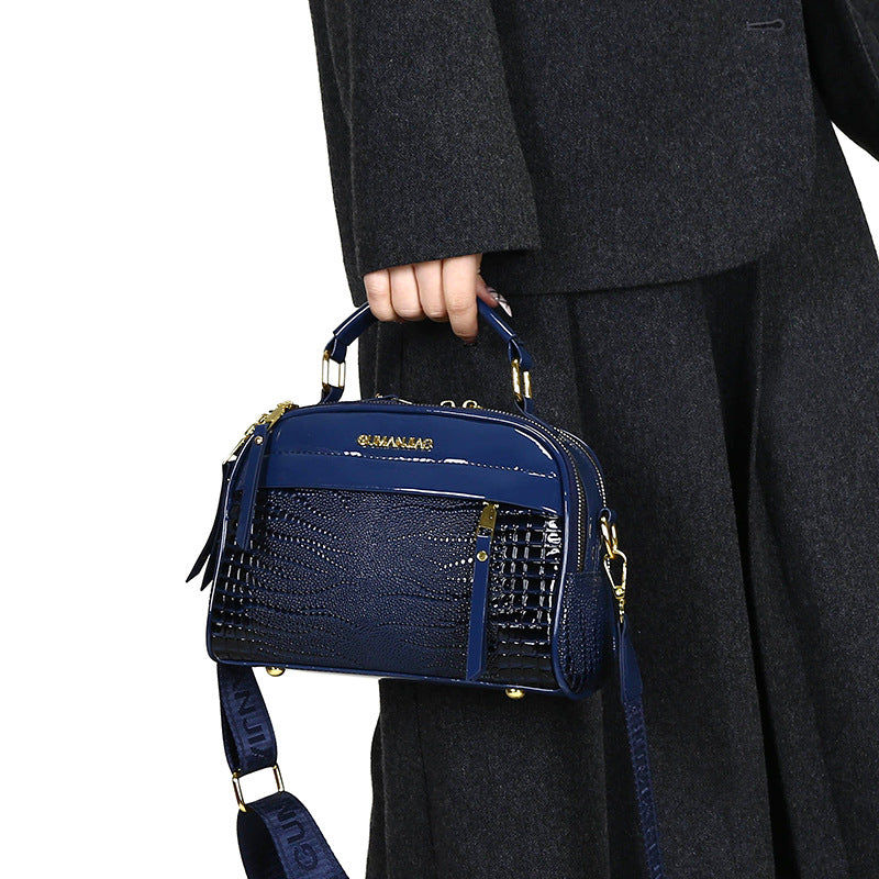 Person holding a blue handbag with a coat in the background