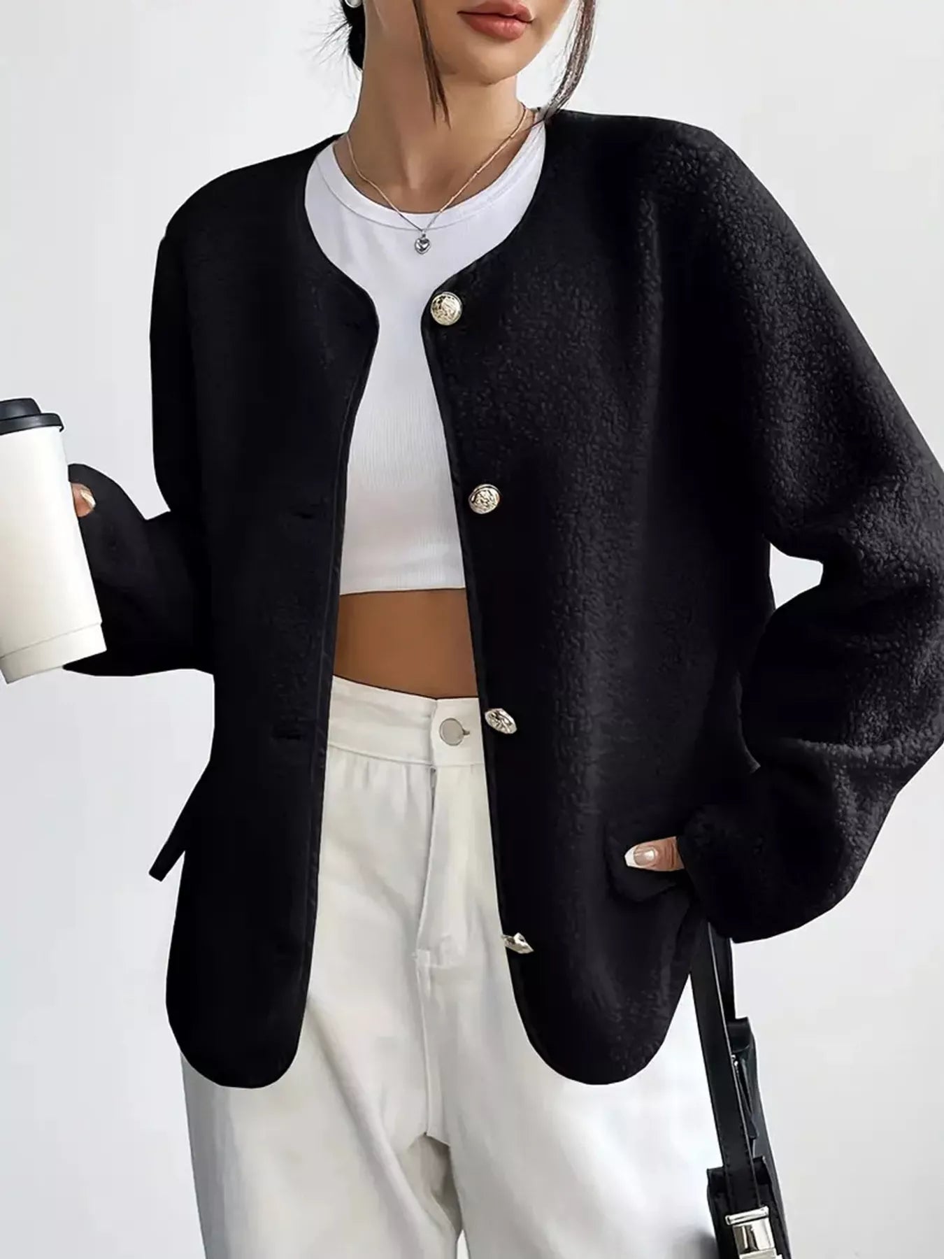 Person wearing a black cardigan over a white top and pants, holding a coffee cup.
