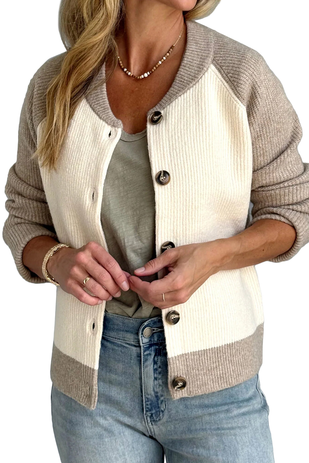 Person wearing a beige and white cardigan with blue jeans on a plain background