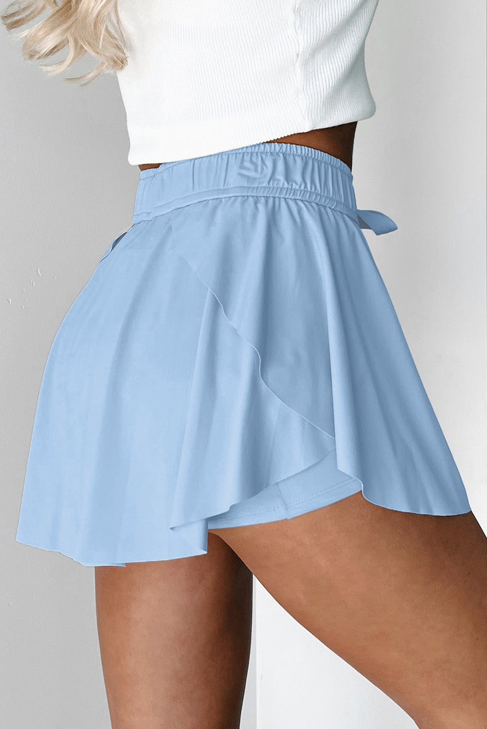 Light blue tennis skort worn by a person on a plain background side view 