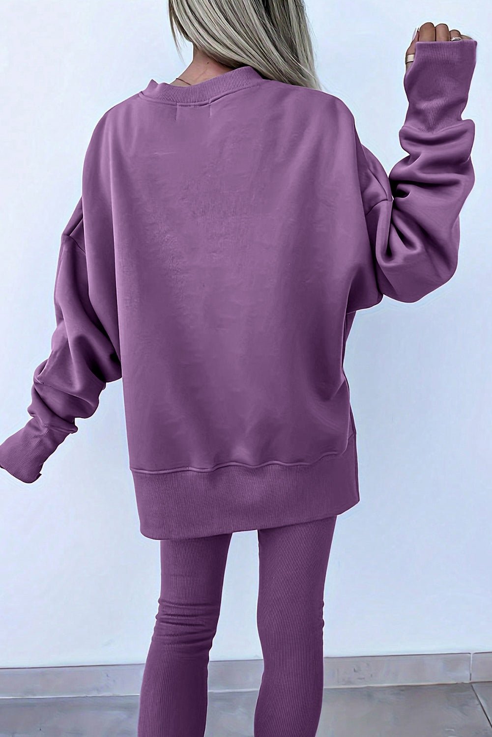 Person wearing a purple sweatshirt and leggings against a white background