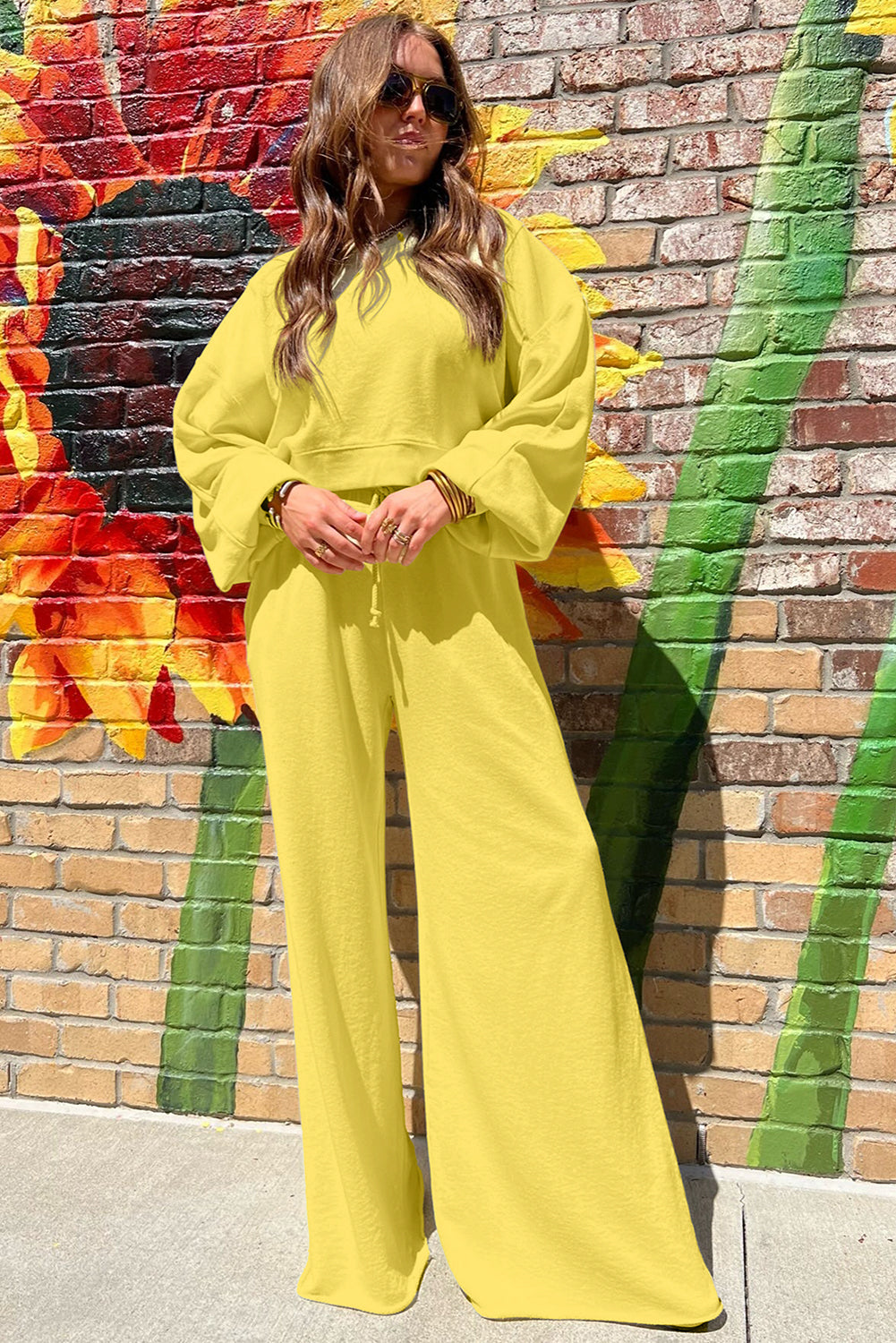 Person wearing a bright yellow outfit standing in front of a colorful mural on a brick wall.