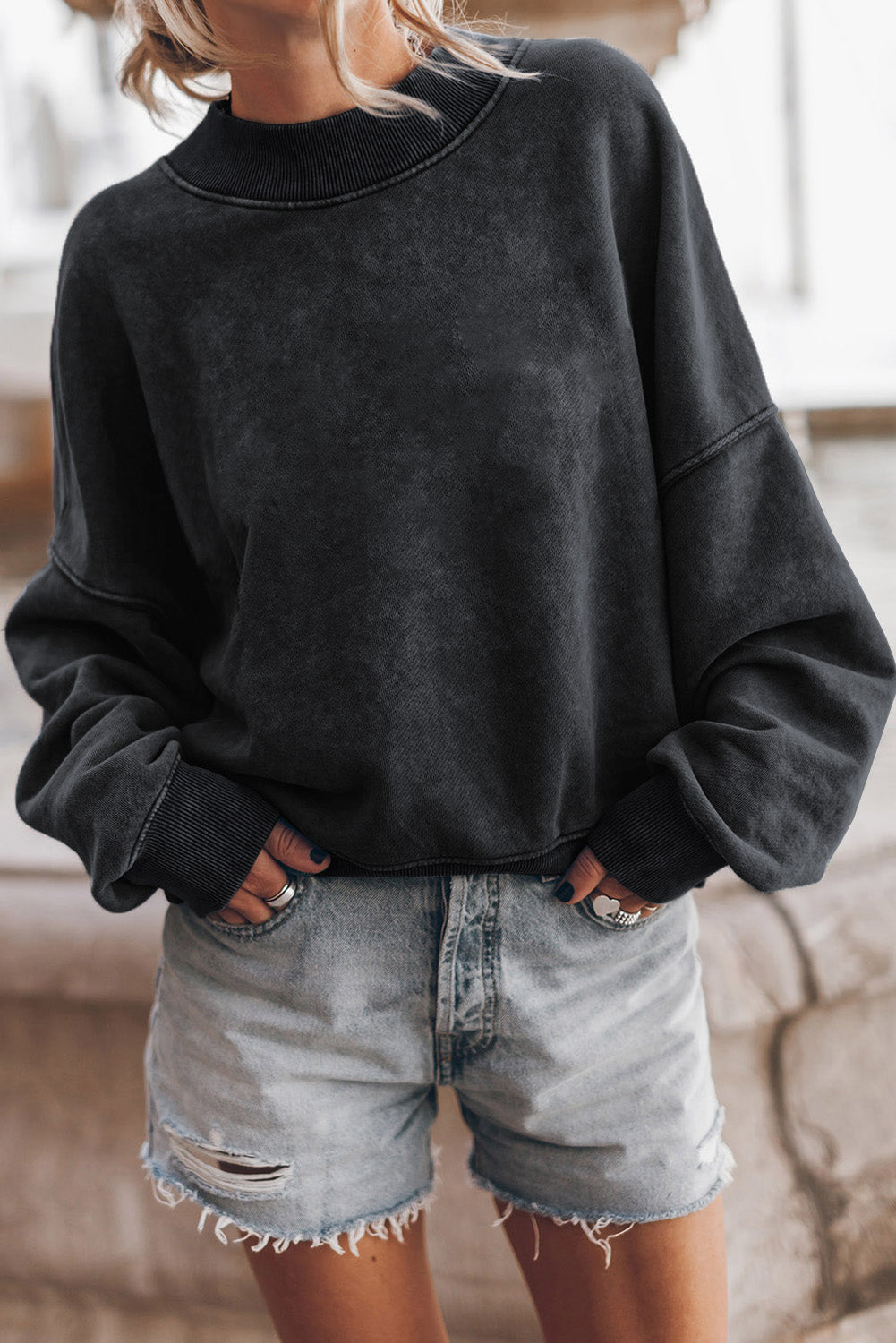 Person wearing a black oversized sweatshirt and denim shorts indoors.
