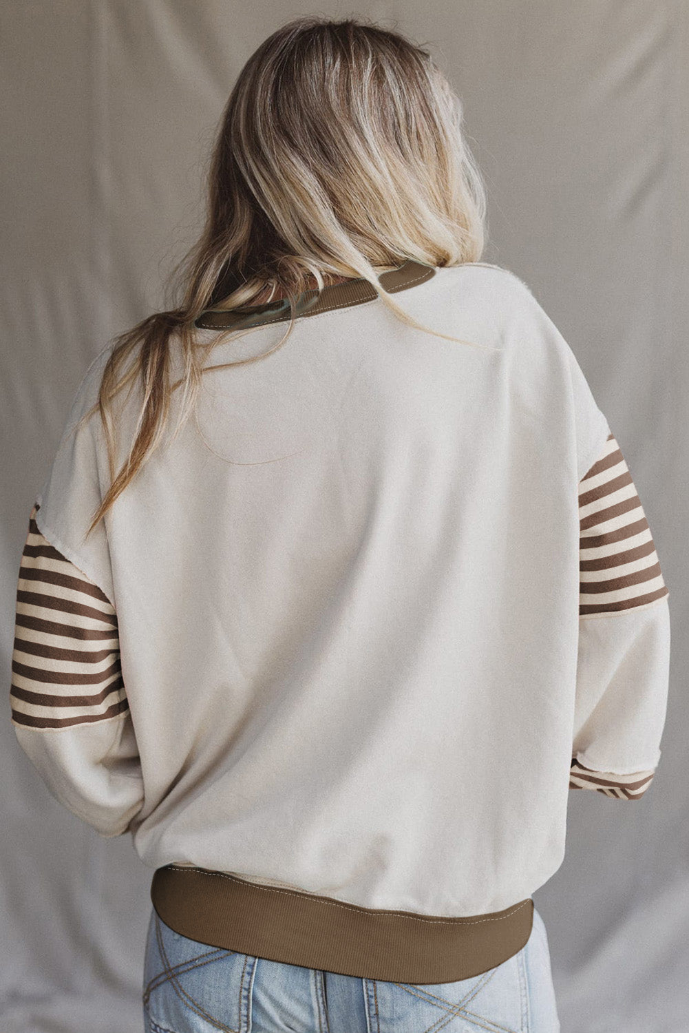 Person wearing a beige sweater with brown striped sleeves against a neutral background